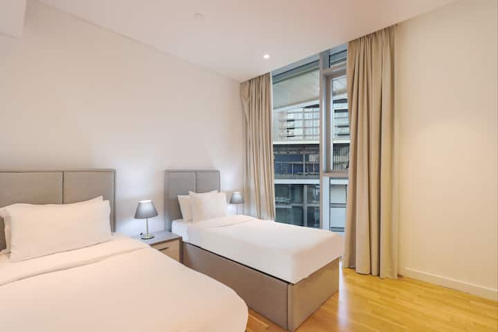 Habitación doble luminosa con dos camas individuales y grandes cortinas de ventana.