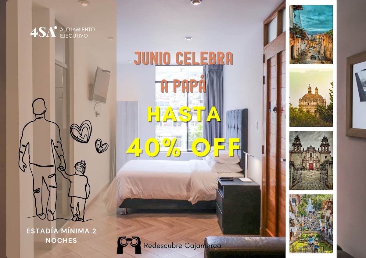 A modern studio apartment features a spacious layout with a comfortable bed and wall-mounted TV. The room is well-lit with natural light, showcasing neutral-toned decor. A welcoming atmosphere is created by the combination of soft furniture and warm wall colors.