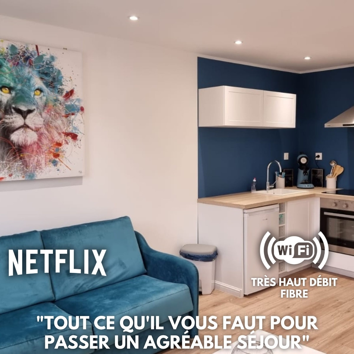 A comfortable living area features a teal sofa with light wood flooring. A modern kitchen is equipped with essential appliances, including a microwave and stovetop. The wall behind the kitchen is painted in a deep blue shade. A decorative lion wall art piece complements the space.