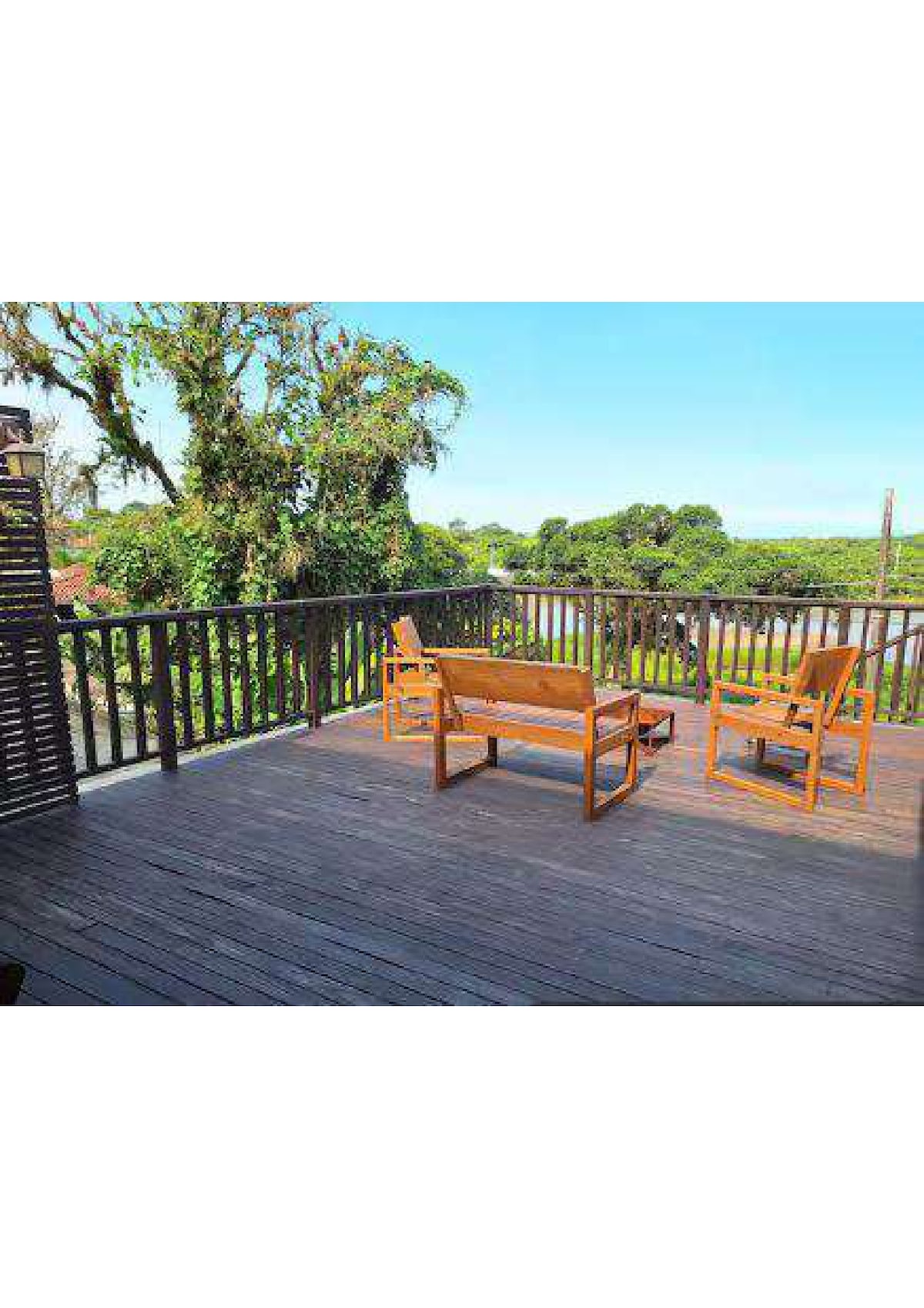 A spacious wooden deck offers seating with two chairs and a bench, providing an outdoor area for relaxation. Lush greenery surrounds the deck, and the open sky above enhances the connection to nature.