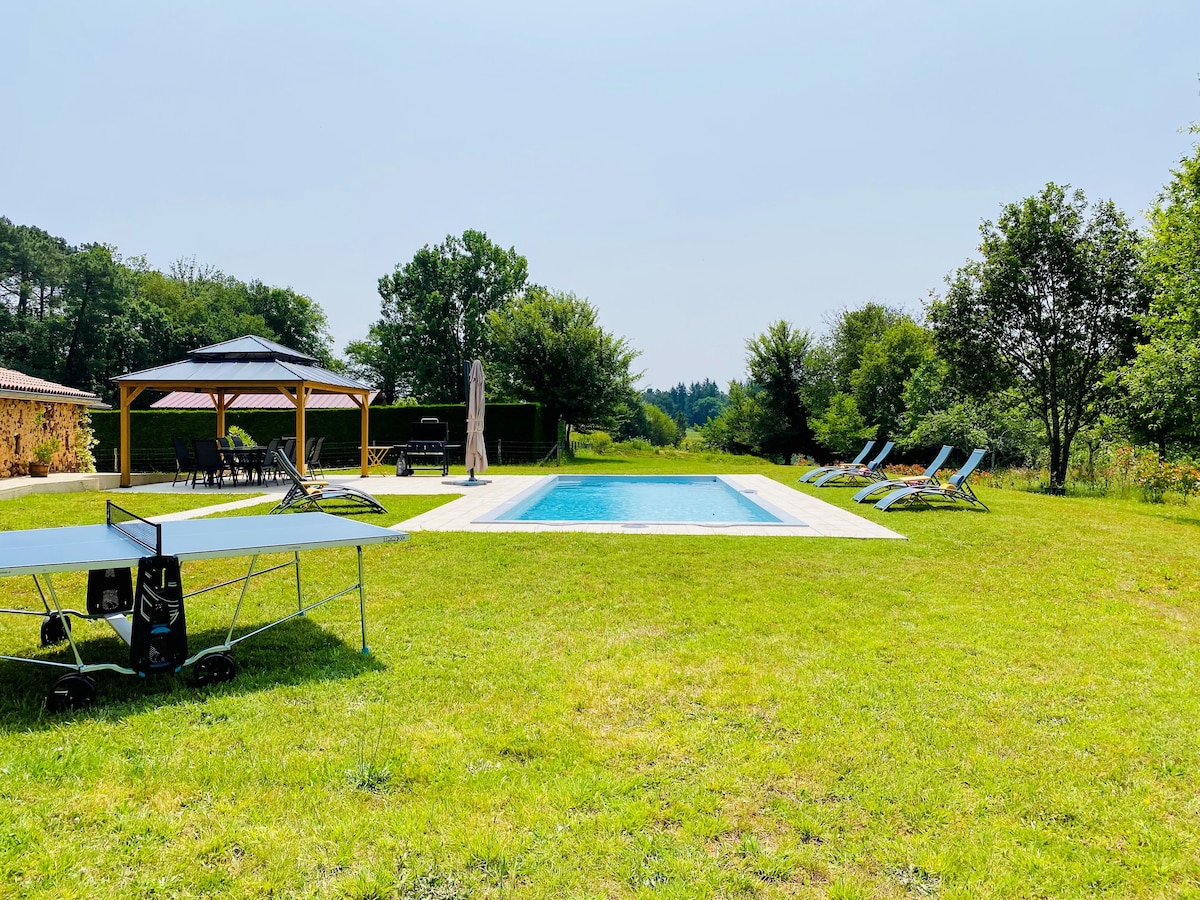 A private heated salt-water swimming pool is surrounded by a lush green lawn. Sun loungers are arranged around the pool, and a gazebo is visible nearby. A table tennis setup can be seen to the left, offering a recreational space amidst the tranquil countryside.