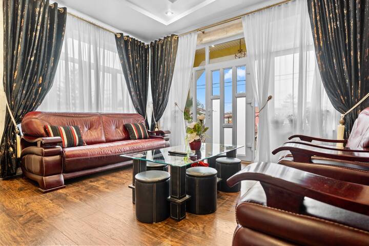 This sophisticated living room offers a blend of classic comfort and modern style, featuring a plush leather sofa, striking high-contrast drapery, and a glass-topped coffee table, creating an inviting space for relaxation and socializing.