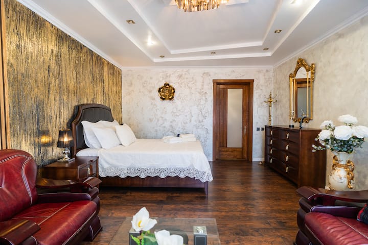 This luxurious bedroom boasts a statement wall, a plush king-size bed with elegant linens, stylish armchairs, and ample storage, creating a serene and opulent retreat.