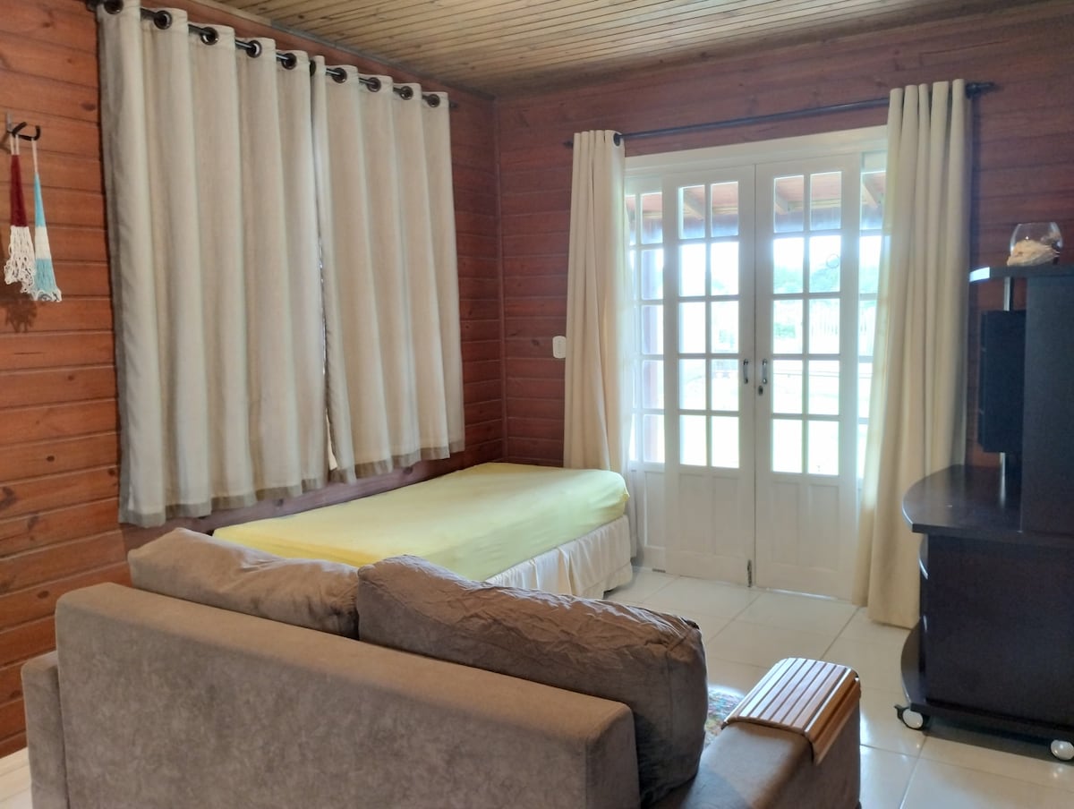 Sala de estar, con sofá, cama y rastrillo. La habitación tiene una puerta al área exterior frente a la casa.