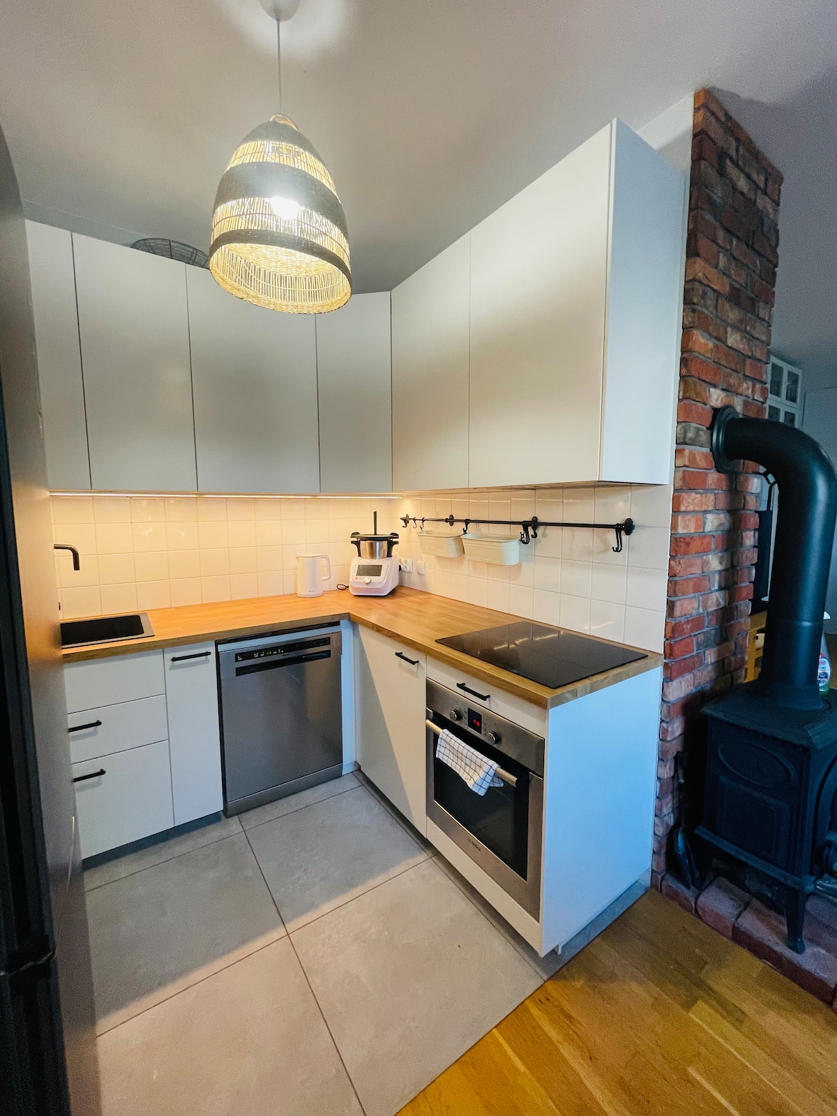 The kitchen is designed with a clean layout featuring white cabinetry and a wooden countertop. A modern induction stove and oven are complemented by stainless steel appliances, including a dishwasher. A stylish pendant light hangs above, and exposed brick adds warmth to the space.