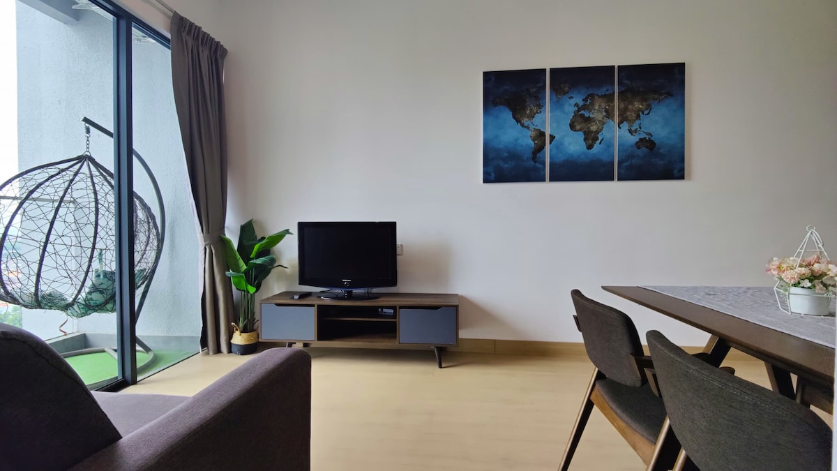 A living area is shown, featuring a flat-screen TV on a contemporary media console. A globe-themed triptych artwork is displayed on the wall. A dining table with dark chairs is positioned nearby, and a hanging chair with a plant adds a cozy element near the balcony doors.