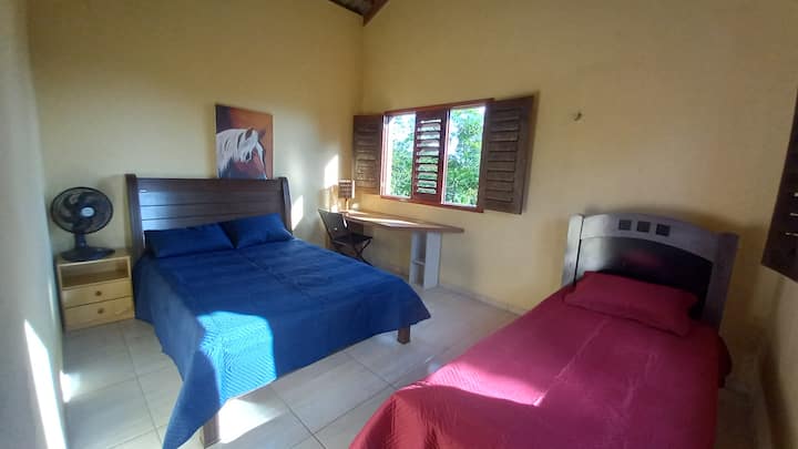 Zeer ruime en luchtige kamer met een tweepersoonsbed, een eenpersoonsbed, een ventilator en twee ramen met een prachtig uitzicht, een ventilator en een tafel en stoel om een soort werkactiviteit te doen met uitzicht op de bergen 