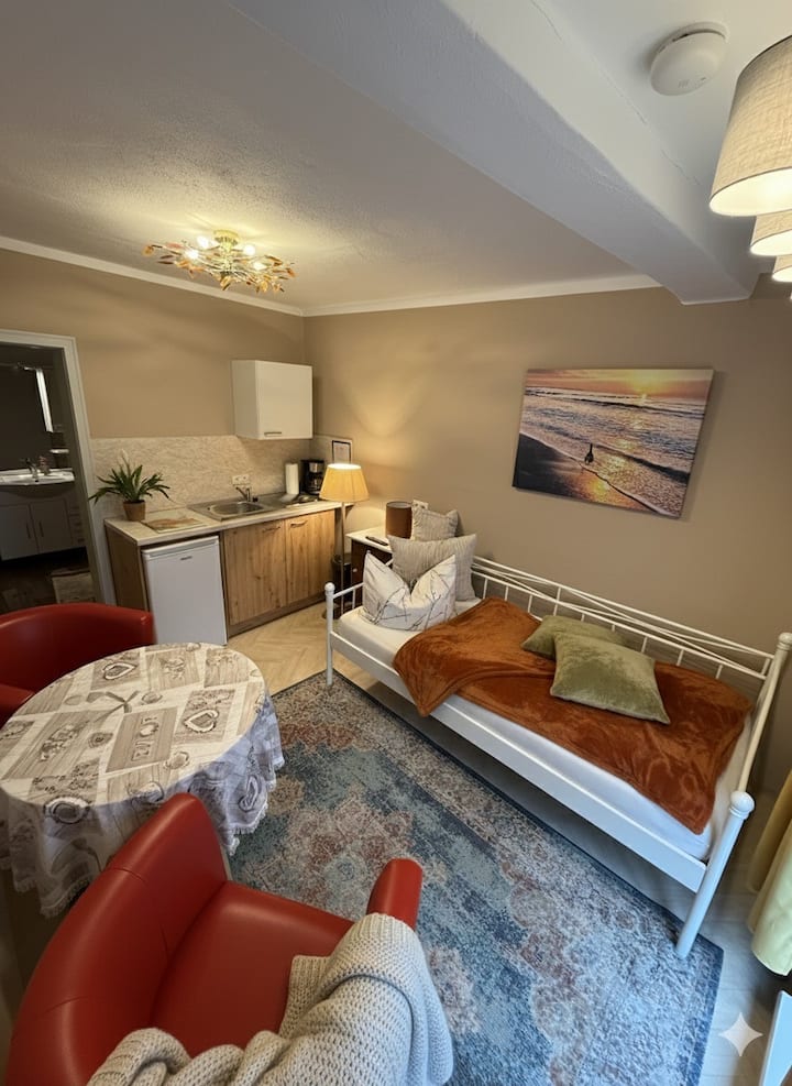 The single room has a single bed, a large floor-to-ceiling window overlooking the courtyard and a small kitchenette. The bathroom is shared with the apartment "Gartenblick."