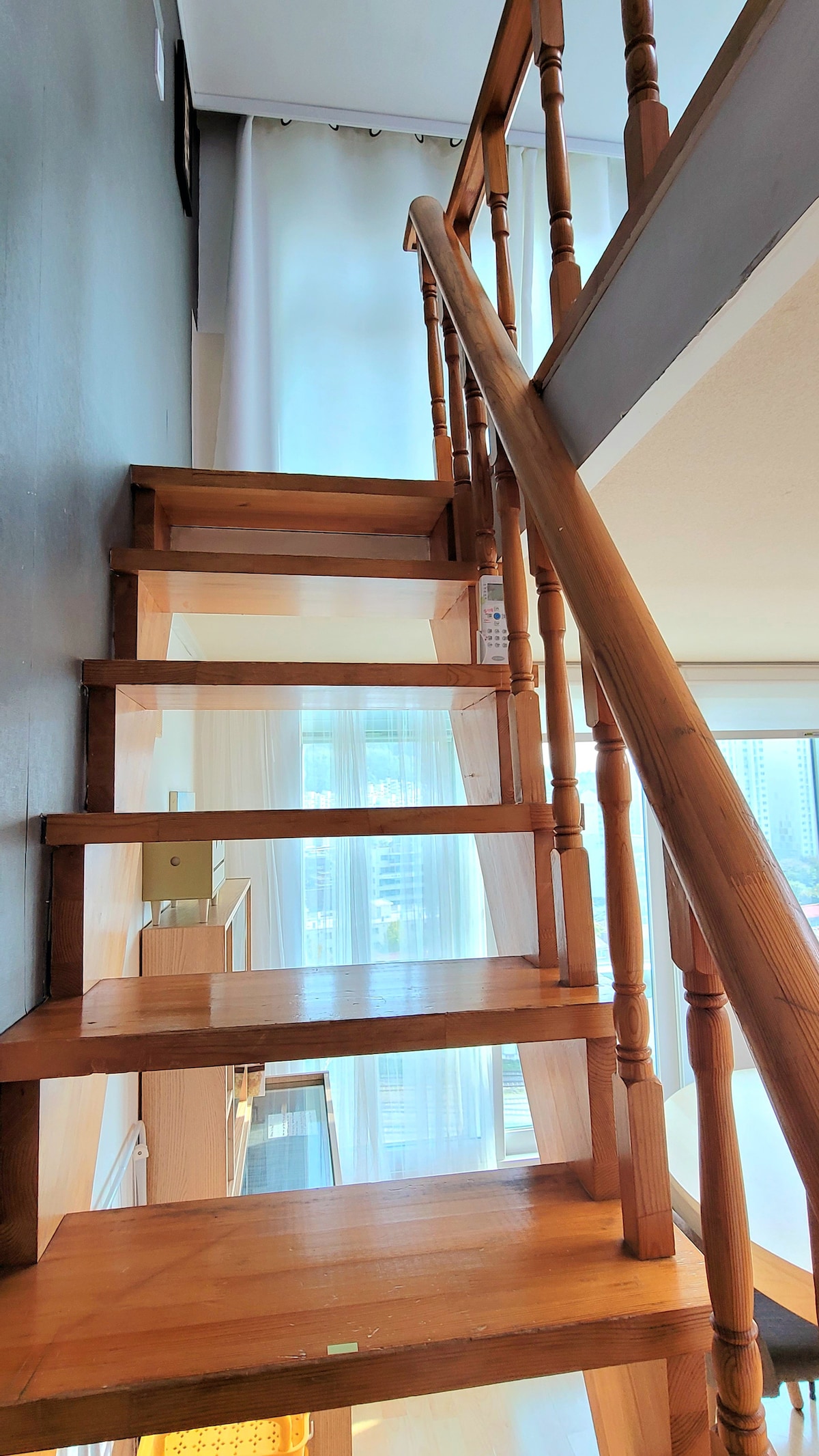 A wooden staircase leads to the upper level, with a light-filled corridor visible through the large windows. The handrails are elegantly designed, and the steps are well-maintained, providing easy access to the second floor.