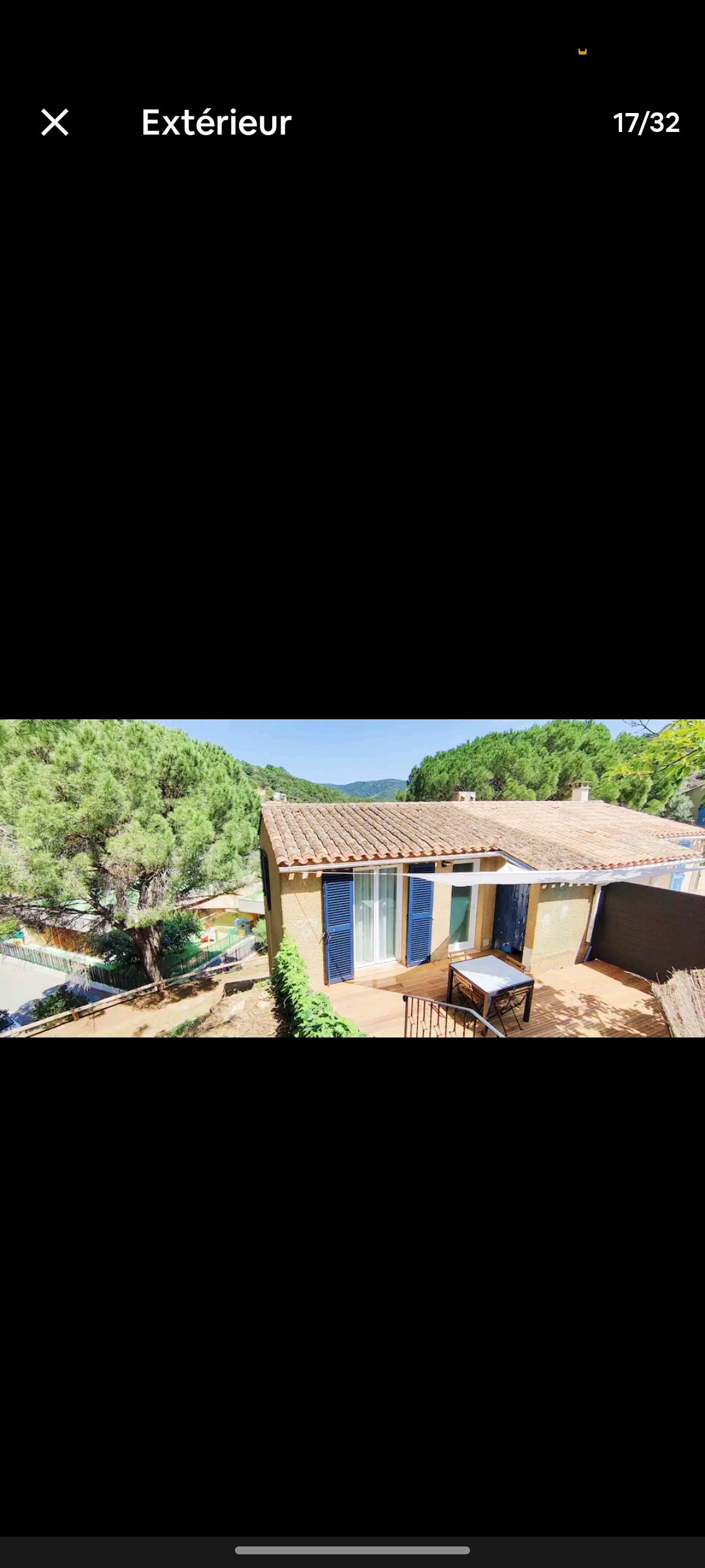 The exterior of the house is presented with a combination of traditional tiles and modern accents. Lush greenery surrounds the property, offering a serene backdrop. Large windows provide views of the landscape, while a terrace area with outdoor furniture invites relaxation.