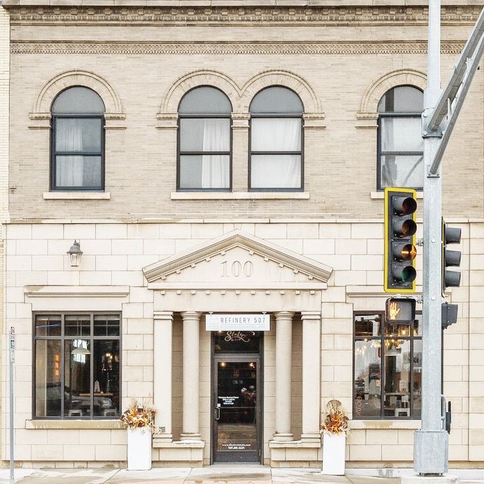The historical building exterior features a decorative façade with large arched windows and a prominent entryway. The entrance is framed by elegant architectural details, while a traffic light stands next to the building, highlighting the busy downtown setting.