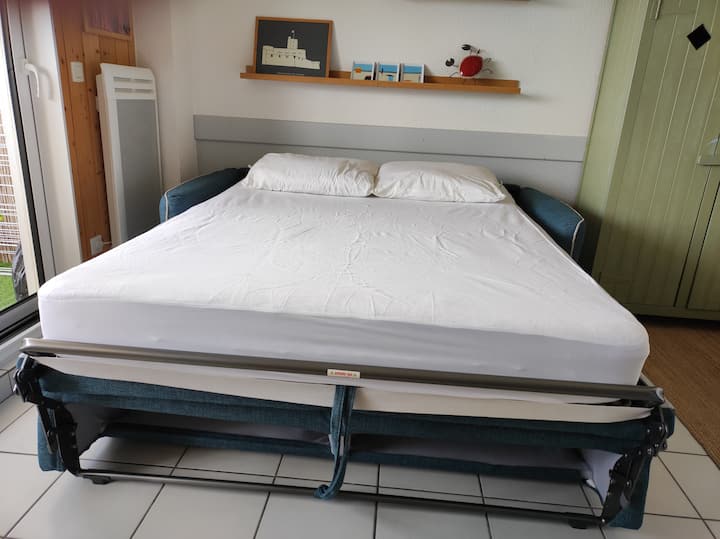 Divan-krevat në dhomën e ndenjjes me dyshek 140 x 190 për 2 persona dhe 2 jastëkë. Kompleti është i mbuluar me një mbulesë mbrojtëse dysheku të papërshkueshme nga uji që ofrohet/shtrojat e krevatit nuk ofrohen.
