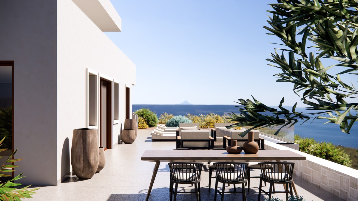 A spacious outdoor terrace is featured, with a dining table and chairs arranged for gatherings. Large planters flank the area. The serene sea view is complemented by lush greenery, providing a peaceful backdrop for relaxation.