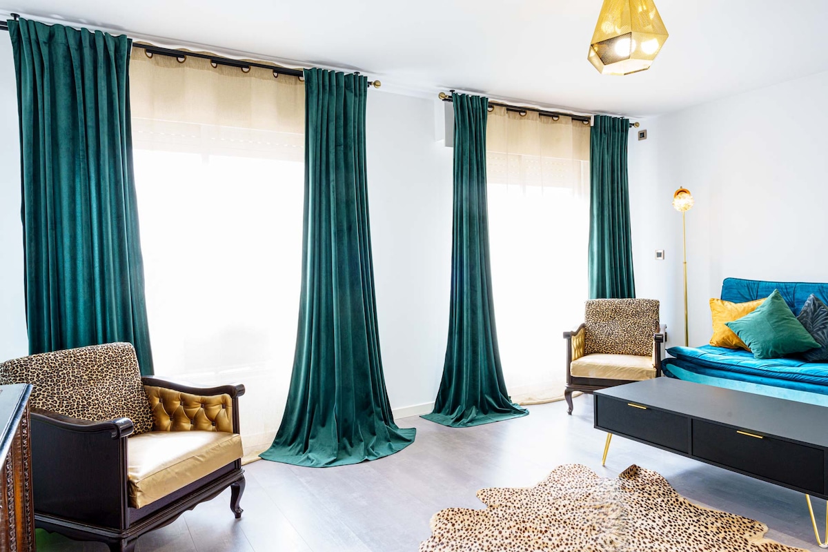 A stylish living area is showcased with two elegant armchairs featuring leopard-print upholstery. Rich teal drapes frame large windows that allow natural light to fill the space. A plush area rug is laid on the floor, adding warmth to the contemporary design.