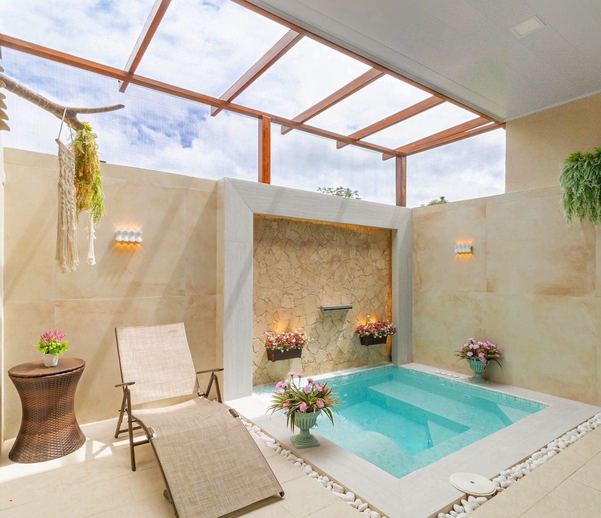 An indoor private jacuzzi is framed by natural stone walls, featuring a clear glass ceiling that allows light to fill the space. Decorative plants provide a fresh touch, while comfortable seating is arranged adjacent to the pool, creating a serene and inviting atmosphere.