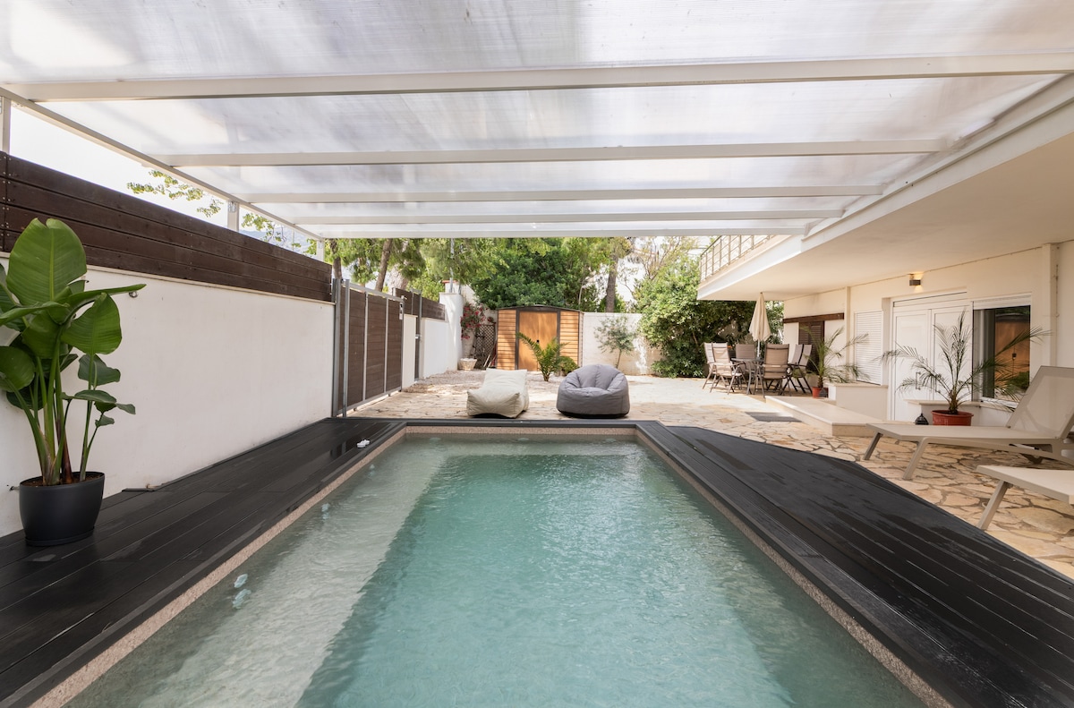 A private outdoor area features a small pool surrounded by stone flooring and a shaded seating area. Sun loungers are placed nearby, while lush green plants add a touch of nature. The space offers a relaxed atmosphere for sunbathing or enjoying a refreshing swim.