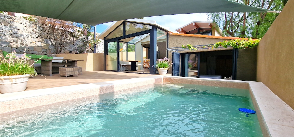 A private pool, measuring 4m x 2.5m, is framed by a wooden deck and surrounded by potted plants. Glass doors of a spacious room provide an open view to the outdoor area, with a shaded seating arrangement situated nearby.