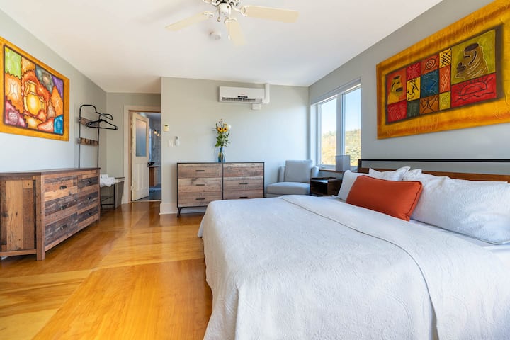 The Dresser room, part of The GristMill Place apartment, features a plush king bed, a skylit bathroom, and calm lake views. The apartment includes a full kitchen, dining room, wood-burning fireplace, and patio, offering a serene, sun-filled retreat.