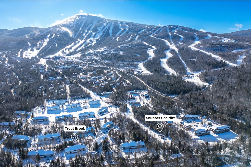 An aerial view captures the snowy landscape surrounding the Sugarloaf area, with the expansive mountain slopes in the background. The Snubber Chairlift is marked, alongside the Trout Brook area, highlighting nearby residential buildings nestled among the trees, creating a serene winter scene.