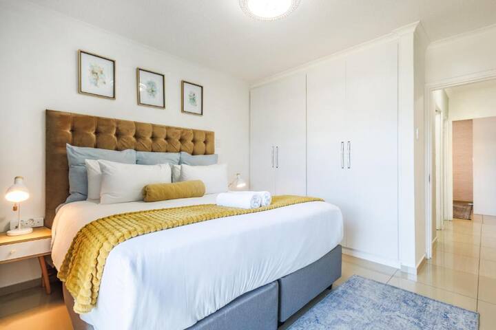 Drift off in this bright, cozy bedroom featuring a king-sized bed with a tufted headboard, soft linens, warm accents, bedside lamps, and ample wardrobe space—perfect for a restful and stylish stay.