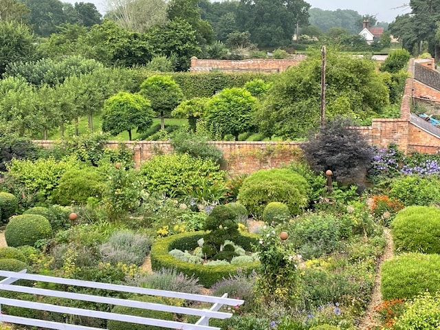 A lush garden is displayed, featuring a variety of greenery, including neatly clipped hedges and flowering plants. A yew maze can be seen among the landscape, enhancing the natural beauty of the surroundings. Sections of vibrant colors create a serene outdoor space.