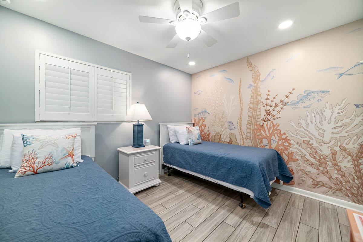 Habitación con 2 camas individuales, un armario con cómoda, un espejo de cuerpo entero, TV inteligente con cable, una máquina de sonido y un altavoz/despertador Bluetooth con puertos de carga.