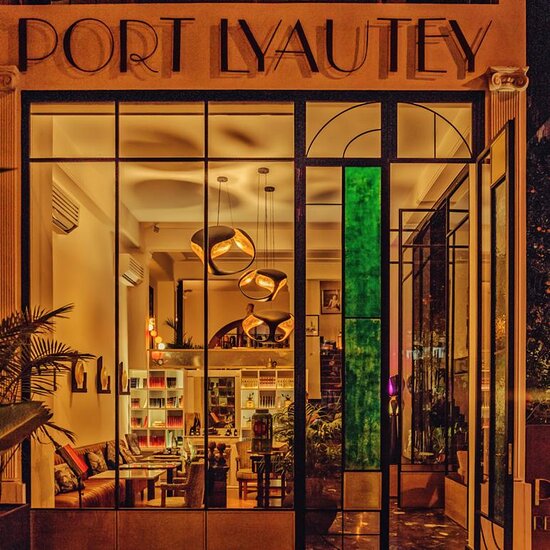 An inviting entrance showcases expansive glass windows that allow soft, warm light to illuminate the space. Unique pendant lights hang from the ceiling, and greenery is placed near the entrance, adding a fresh element to the inviting environment.