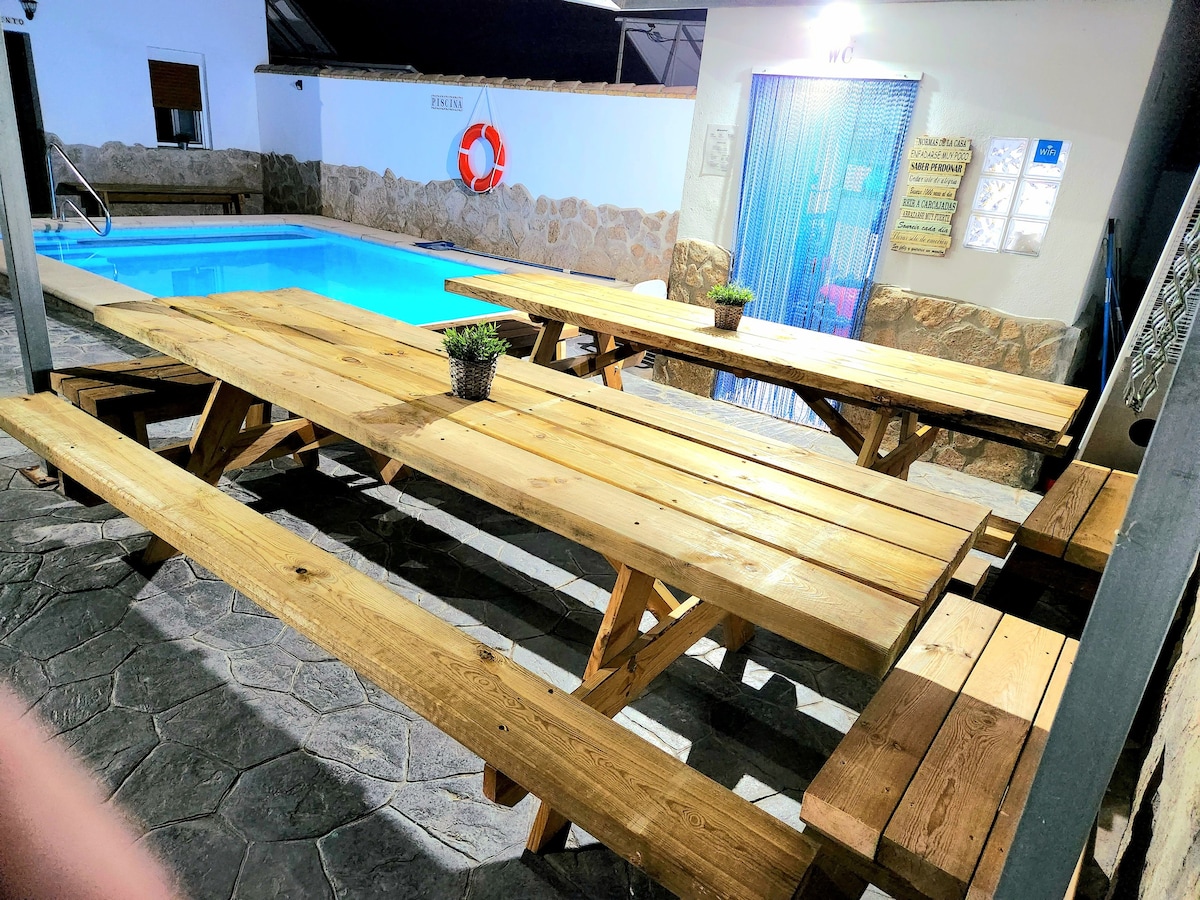 A spacious outdoor dining area is equipped with wooden picnic tables, providing ample seating for guests. A private pool glistens nearby, complementing the relaxed atmosphere. On the walls, safety and facility signage is prominently displayed.