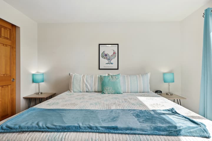 Fresh linens on the king bed reflect the light and airy decor. Bedside tables feature lamps with USB charging ports. 