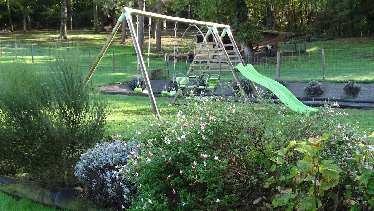 A playground area is visible with a wooden swing set and slide set against a backdrop of a green lawn. Colorful plants border the area, adding a touch of greenery. The playground is enclosed with a wooden fence, providing a safe space for children to enjoy.