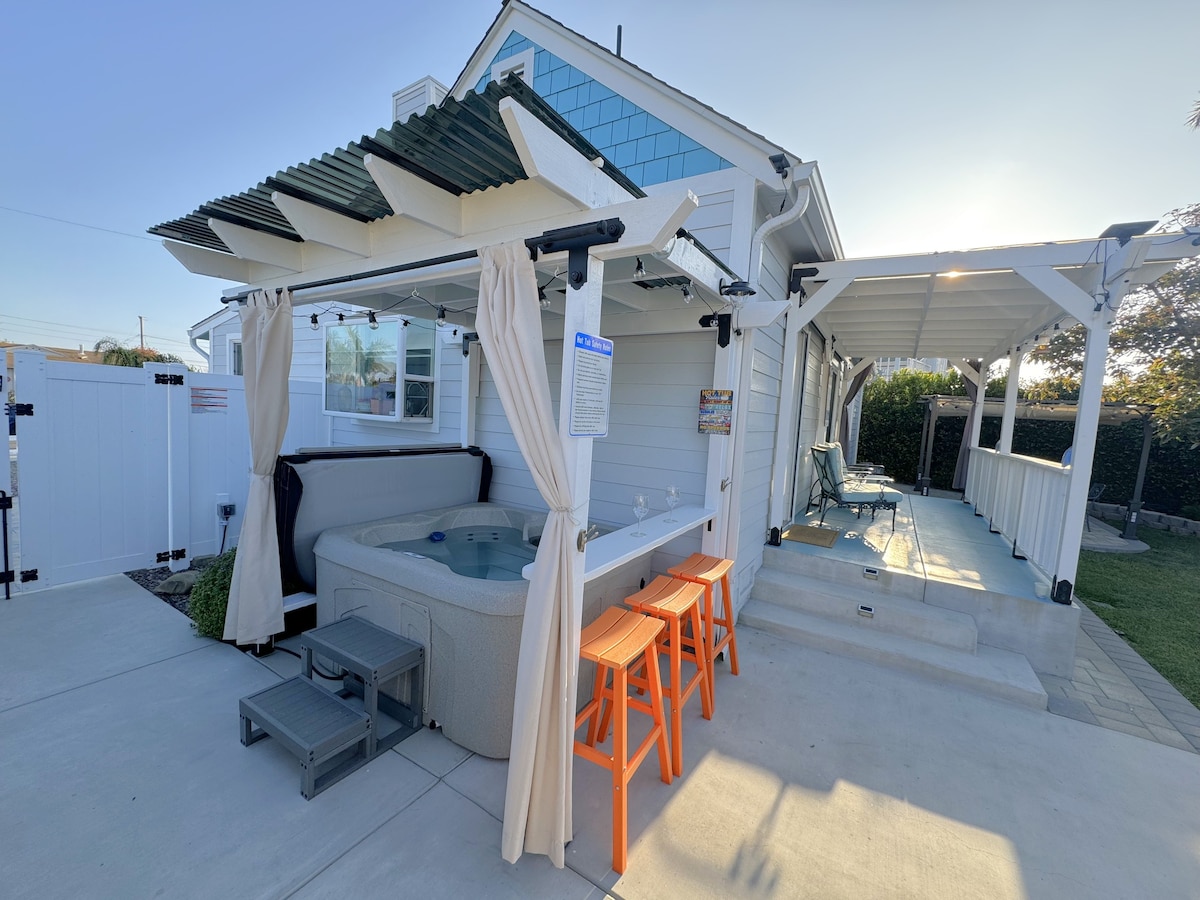 An outdoor area features a hot tub surrounded by a privacy fence and lounge furniture. Nearby, two barstools provide seating at a counter. A patio space is accessible, and a covered area offers shade, enhancing the functionality of this inviting outdoor environment.