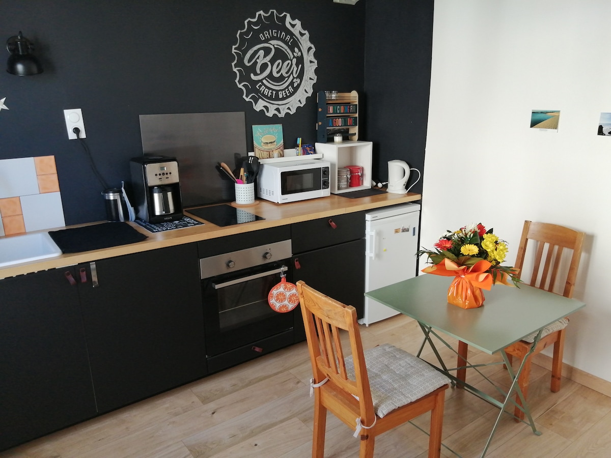 The kitchen area features a compact layout with dark cabinetry and a light countertop. A coffee maker, microwave, and compact refrigerator are present. A small dining table with two wooden chairs is adorned with a vibrant bouquet, adding a touch of color to the space.