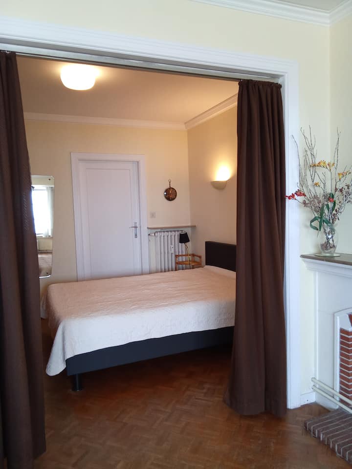 Спалня с двойно легло, затворена със затъмняващи завеси, с директен изглед към банята от едната страна, всекидневната от другата