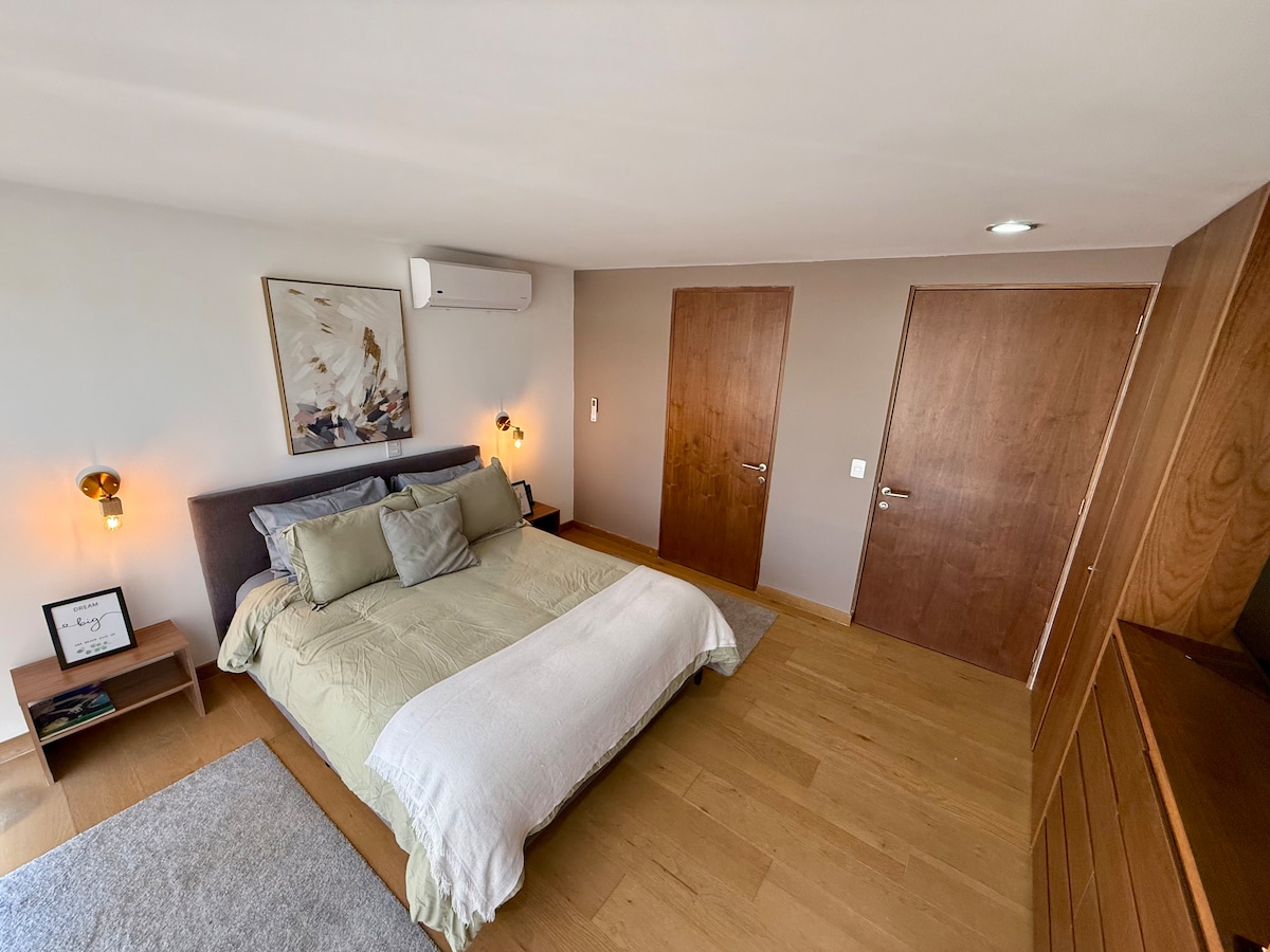 Chumba kizuri cha kulala chenye mapazia ya rangi nyeusi, furahia mapumziko matamu katika kitanda hiki cha Queen chenye starehe sana na uchague mto unaoupenda zaidi, kina televisheni na bafu kamili la kujitegemea. 