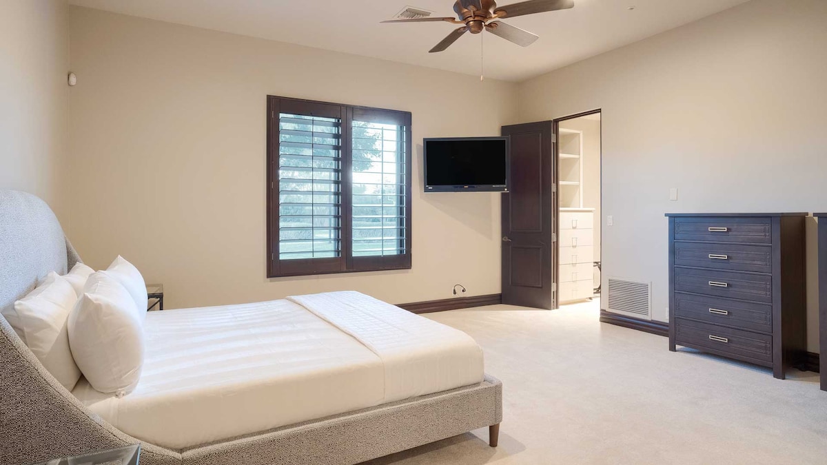 Moderna spavaća soba sa svijetlosivim krevetom, zidovima u neutralnoj boji, otvorenim vratima ormara i prirodnim svjetlom.