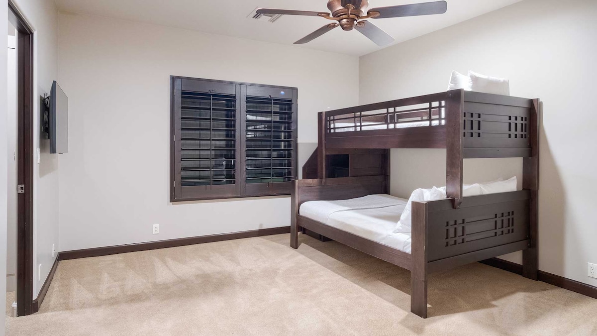 Funkcionalna spavaća soba s krevetom na kat od tamnog drva, bijelom posteljinom, televizorom na zidu i prirodnim svjetlom.