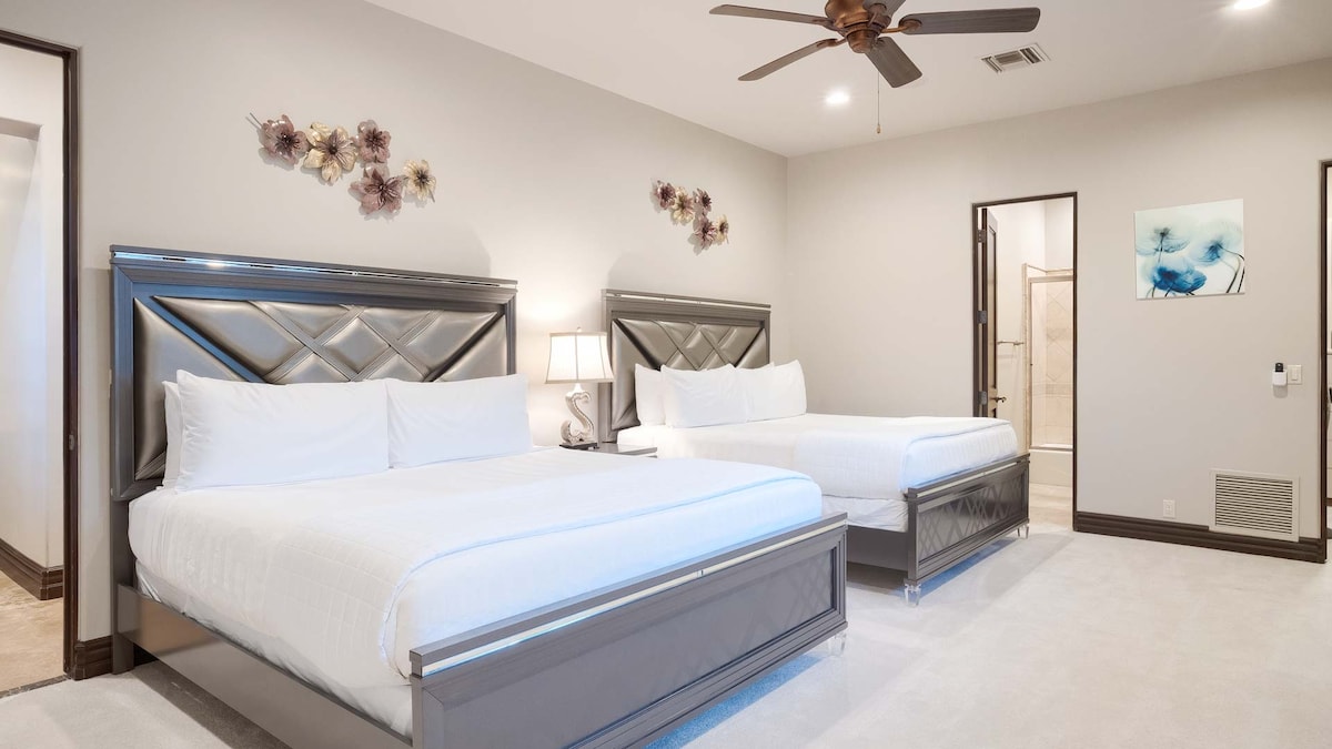 Ovo je čista, moderna spavaća soba s kupaonicom i dva kreveta, od kojih je svaki uredno namješten s bijelom posteljinom i ukrasnim jastucima. 