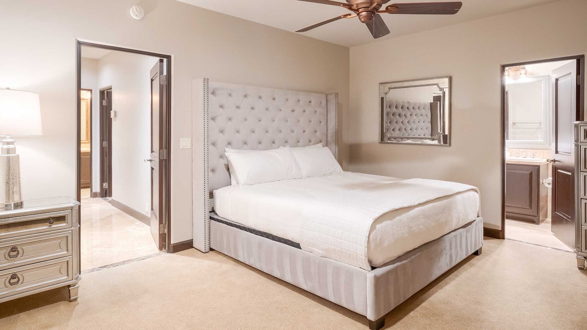 Udobna spavaća soba sa svijetlosivim uzglavljem, stolićima, kupaonicom i hodnikom koji je povezuje s drugim prostorijama.