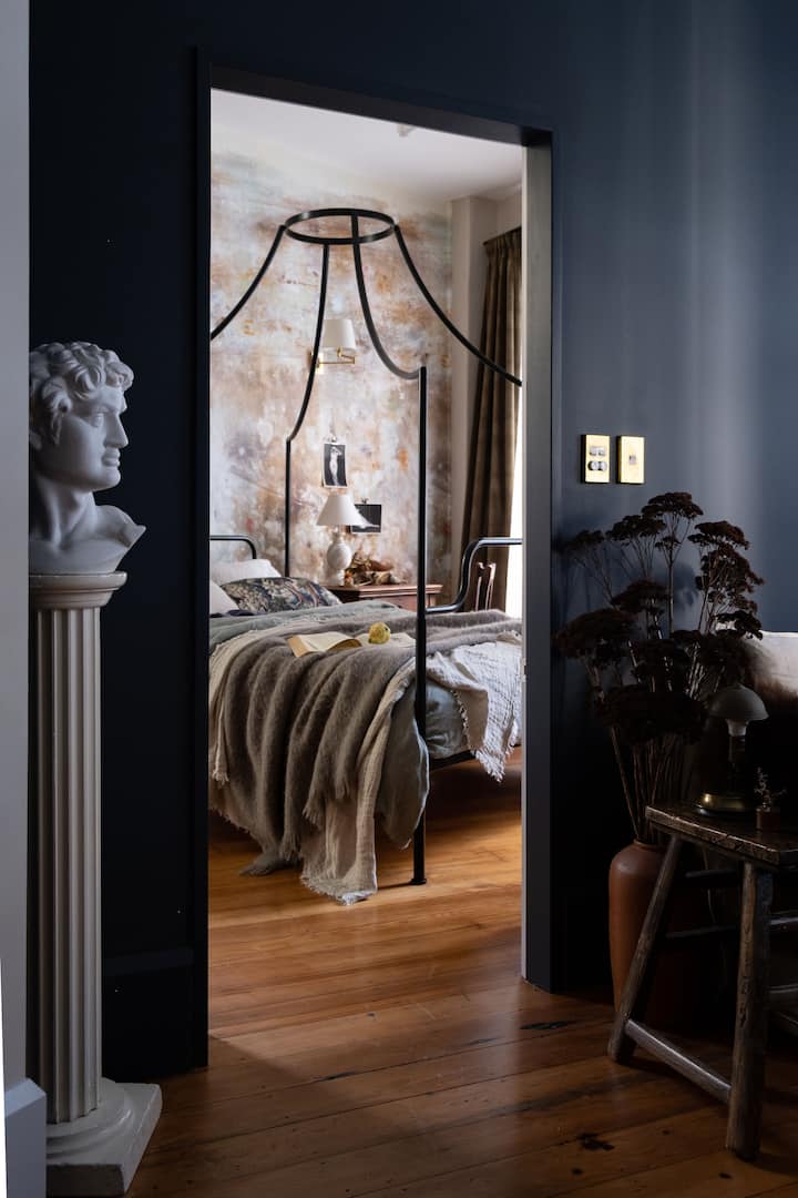 Moody bedroom with dark walls, a canopy bed draped with cozy blankets, and decor featuring classical and vintage elements