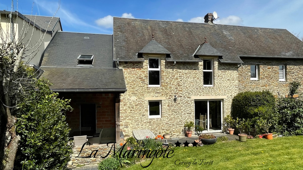 The rustic stone facade of a two-story house is framed by a well-maintained garden. Large glass doors provide a view into the living space, while a small patio area invites outdoor relaxation. The roof is gently sloped, enhancing the charming appearance.