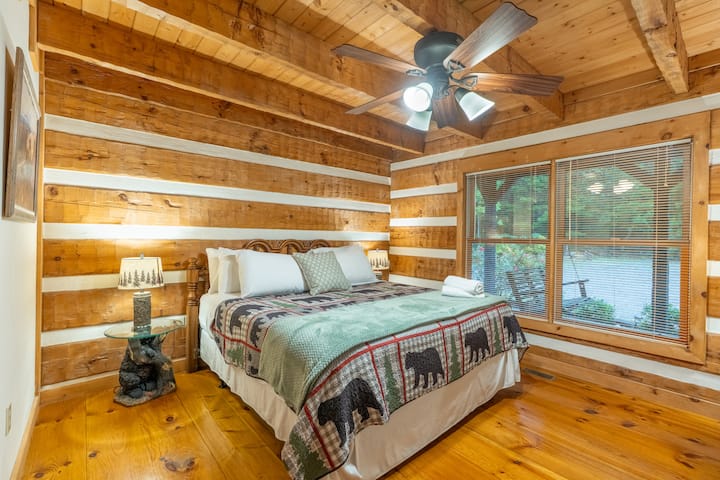 Main-level king suite with large windows showcasing front porch views. Thoughtfully appointed with lighted closet storage, dresser, TV, and ceiling fan.
