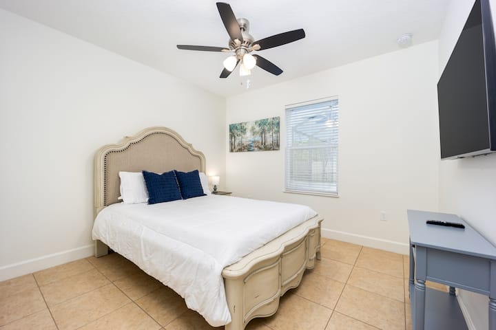 Chumba cha kulala #2 kina kitanda cha ukubwa wa Malkia, meza ndogo ya usiku, taa ndogo, TV janja ya 50", meza ya kuhifadhi, na mwonekano wa bwawa.