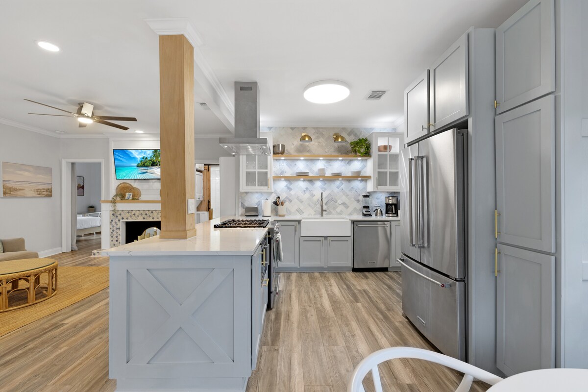 A spacious kitchen is presented, featuring a central island with a clear countertop and modern appliances. Light grey cabinetry complements the design, while hexagonal backsplash tiles add texture. Pendant lighting hangs above, illuminating the workspace. Open shelving showcases decorative items and kitchen essentials.