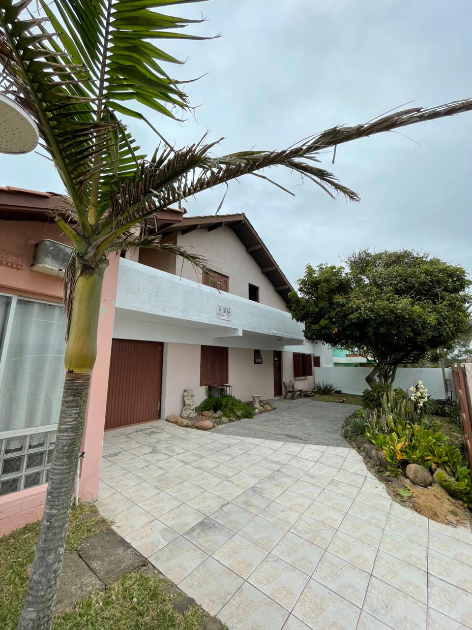The exterior of the house features a landscaped entrance with a tile driveway, bordered by a variety of plants and foliage. A palm tree adds a tropical touch, while the two-story structure showcases a covered porch and a garage space.