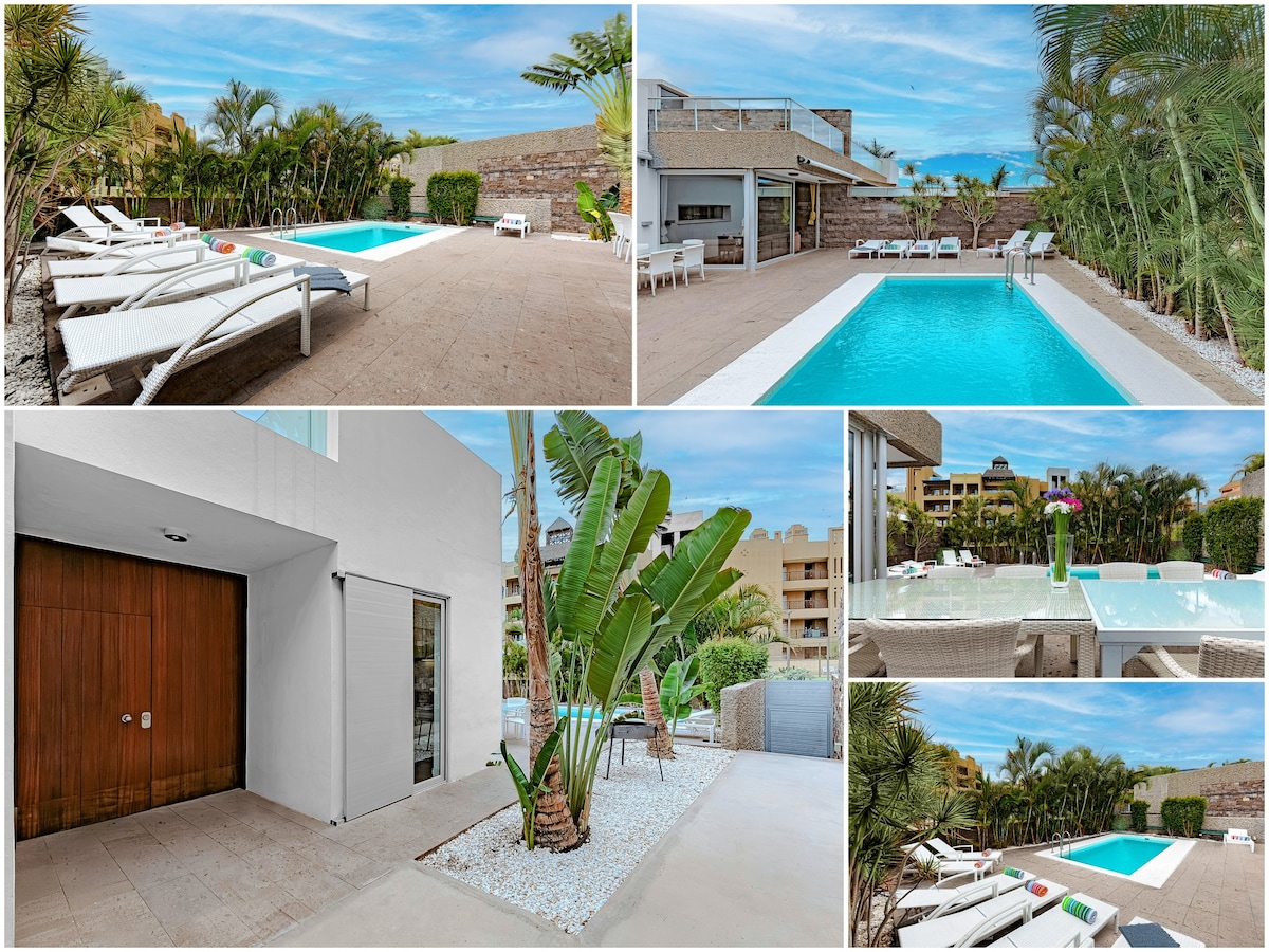 The outdoor area features a private heated swimming pool surrounded by a spacious patio. Sun loungers are positioned alongside the pool amidst tropical plants. A dining area with a table and chairs is visible, ideal for enjoying meals outdoors. A barbecue station is also present for guest use.