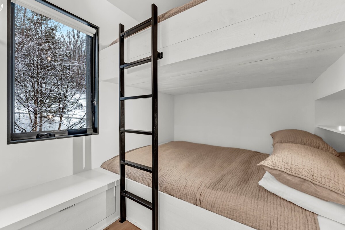 Krevate dopio "queen" në katin e sipërm të dhomës së gjumit me rafte të ndërtuara; shtroja belge nga Restoration Hardware, të ndërtuara në stola dhe sirtarë.