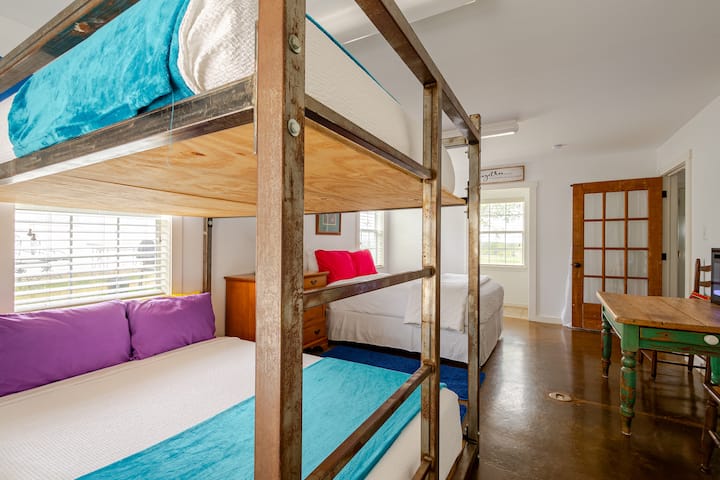 Check out this unique, steel-framed queen-sized bunk bed that accommodates 4 people, with an additional queen-size bed next to it. The view includes the entrance to the attached half bath. This room is ideal for larger groups and families with kids!