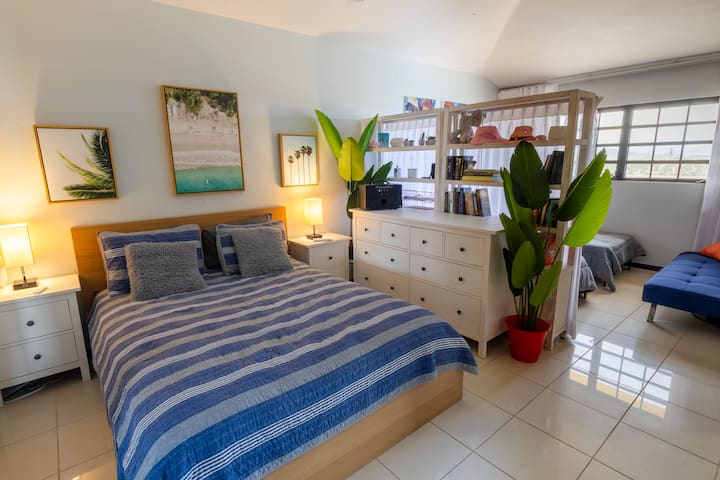 "Chumba kirefu cha kulala" kilicho na Kitanda cha Malkia upande wa kushoto, kimetenganishwa na vitanda viwili pacha upande wa kulia kabisa na sanduku la vitabu lililoungwa mkono na pazia jeupe lenye shuka nusu.