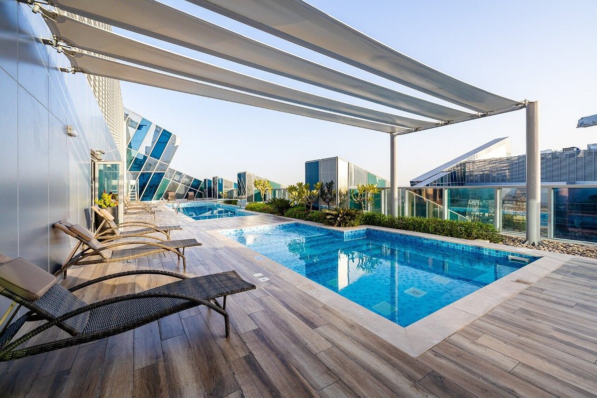An outdoor pool area is displayed with two separate swimming pools, surrounded by neatly arranged lounge chairs. Sunshade canopies provide shelter, while modern buildings are visible in the background, enhancing the serene setting for relaxation and leisure.