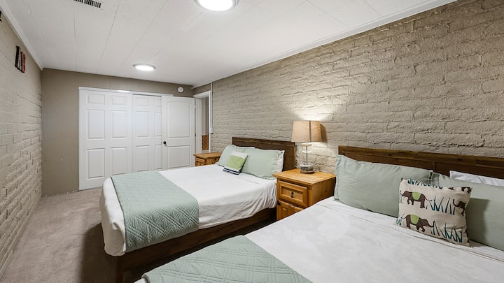 חדר שינה במרתף מזמין עם שתי מיטות נפרדות, קיר לבנים ותאורה רכה.